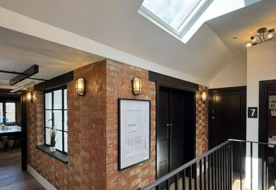 Bright upper-level hallway with brick walls, black metal railings, and a large skylight.