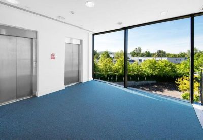 Elevator landing with blue carpeting and floor-to-ceiling windows showing leafy outdoor views.