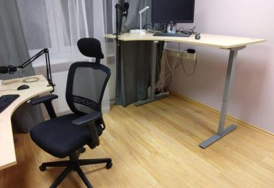 Height-adjustable corner desk and ergonomic mesh chair in a bright workspace.