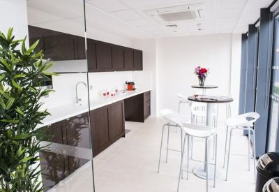 Modern communal kitchen area with dark wood cabinetry and white bar seating.