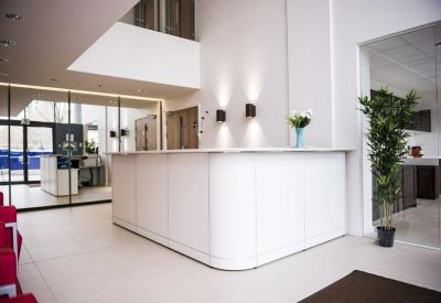 Minimalist white reception desk in a bright, open lobby with potted plants.