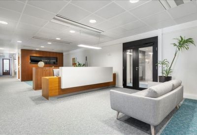 Spacious reception area with a sleek white desk, grey sofa, and large glass doors.