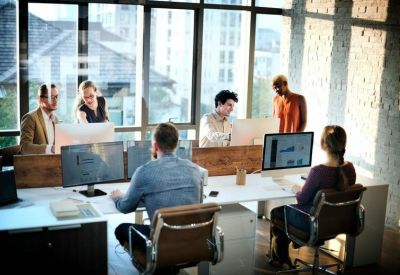 Lively coworking space with people working at desks in a room with exposed brick and large windows.