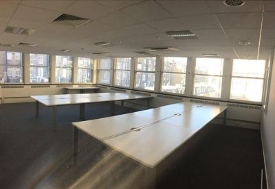 Open-plan workspace featuring long white desks and large windows for natural light.