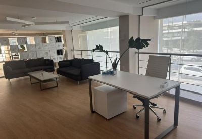 Office area with desk, black sofas, and large windows providing natural light.