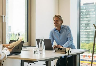 Modern office workspace with a man standing at a height-adjustable desk near a large window.