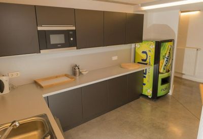 Modern communal kitchen area with dark cabinetry and a green vending machine.