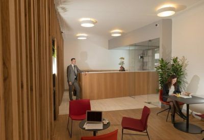 Modern lobby with red chairs, wood-paneled walls, and a reception desk in the background.