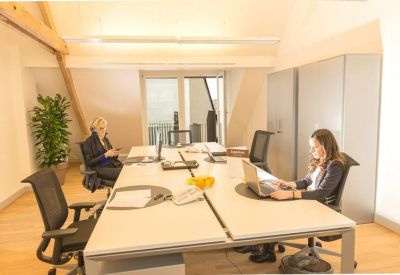 Bright open-plan office suite featuring white desks, black chairs, and natural wood accents.