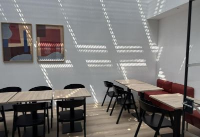Coworking dining area with wooden tables, black chairs, and sunlight patterns on the walls.