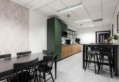 Modern office kitchen with green cabinetry, wooden accents, and a high-top dining table.