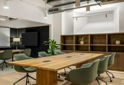 Bright conference room with a large wooden table, green swivel chairs, and built-in shelving.