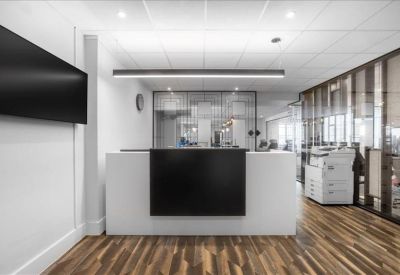 Minimalist reception area with a sleek white desk and wood-effect flooring.