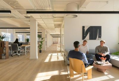 Spacious communal lounge with people on a sofa and a wooden armchair under warm natural light.