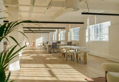 Bright open-plan workspace with long white desks and large windows overlooking the street.