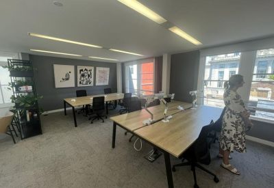 Modern open-plan office with wooden desks, black chairs, and framed artwork.