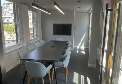Meeting room with a long dark table, grey chairs, and a wall-mounted screen.