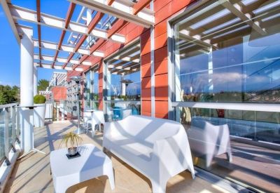 Sunlit outdoor terrace with white lounge furniture and wooden pergola.