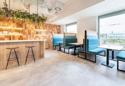 Modern communal cafe area with wooden paneling, hanging plants, and teal blue booth seating.