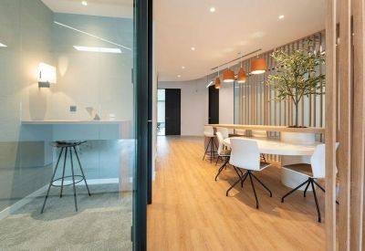 Bright coworking area with a high-top wooden table, white chairs, and an olive tree.