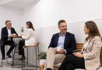 Coworking members chatting over coffee in a bright breakout area with wooden benches.