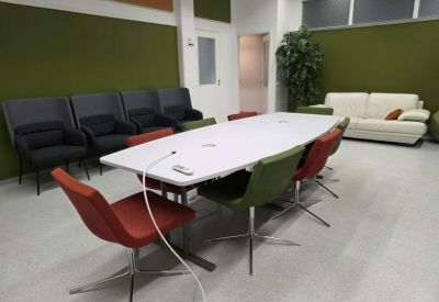 Conference room with a long white table, colorful chairs, and a white sofa.
