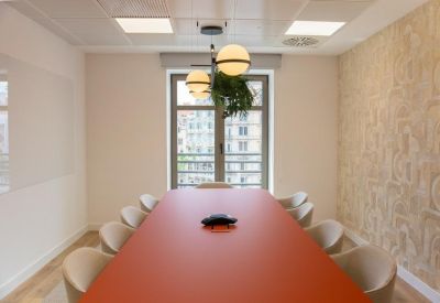 Meeting room with a long orange table, neutral chairs, and a hanging plant feature.