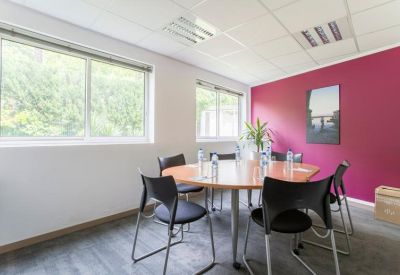 Meeting room with round table, black chairs, and a pink accent wall.