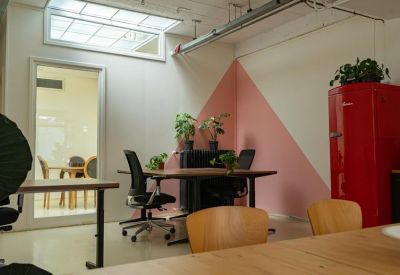 Workspace with wooden desks, black office chairs, and a red retro refrigerator against a pink geometric wall.