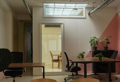 Meeting area with wooden tables and chairs situated under a skylight and industrial piping.
