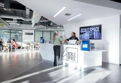 Bright reception area with a white desk, large logo, and a spacious lobby with people.