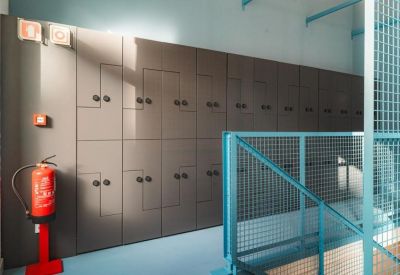 Storage area with grey lockers and a red fire extinguisher next to a blue metal railing.