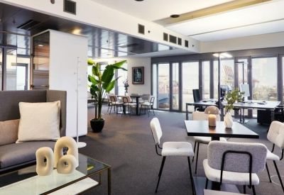 Contemporary breakout lounge with a plush grey sofa, white chairs, and a large potted plant.