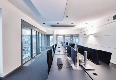 Long open-plan office with grey desks and ergonomic black chairs along a window wall.