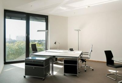 Bright office room featuring a large shared desk and floor-to-ceiling windows.