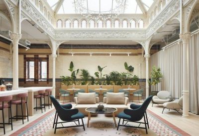 Grand communal lounge under an ornate white skylight with teal armchairs and indoor plants.