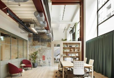 Double-height creative workspace with white desks, red armchairs, and exposed industrial details.