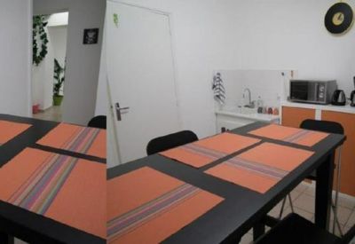 Communal kitchen and dining area featuring a black table with orange placemats and a grey refrigerator.