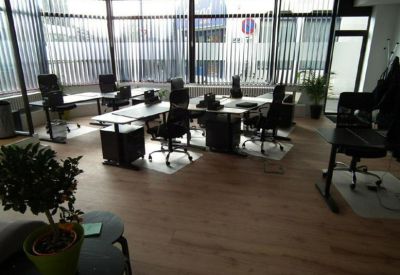 Spacious open-plan workspace with multiple desks, office chairs, and large windows with blinds.