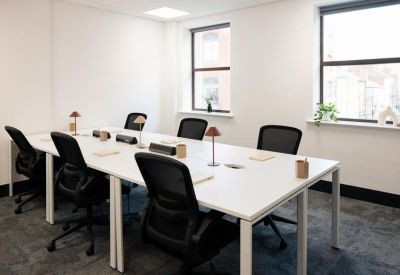 Bright shared workspace with two large windows and several white workstations.