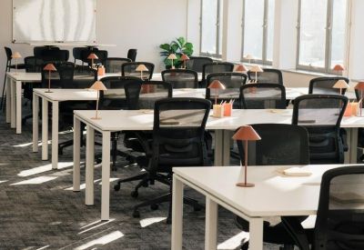 Spacious open-plan office featuring rows of white desks and desk lamps under bright lighting.