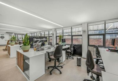 Bright open-plan workspace with white desks, ergonomic chairs, and indoor plants.
