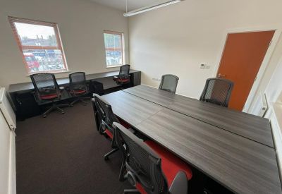 Bright office with a long dark wood desk, ergonomic chairs, and natural light from two windows.