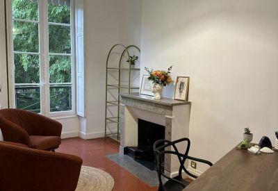 Bright workspace at 6, Rue de la Monnaie with velvet armchairs, a fireplace, and garden views through tall windows.