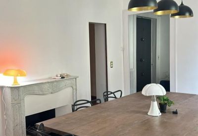 Communal dining and meeting area featuring a large wooden table, designer black chairs, and a classic fireplace.