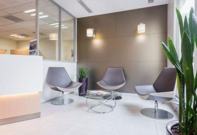 Modern reception waiting area with stylish grey armchairs and a glass coffee table.