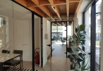 Bright hallway with glass walls, exposed wooden ceiling beams, and indoor greenery.