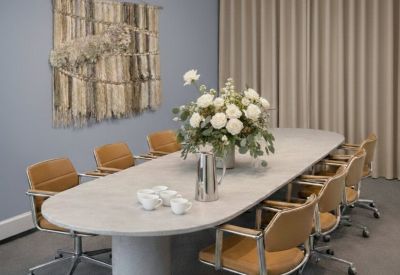Meeting room with an oval concrete table, tan leather chairs, and two large globe chandeliers.