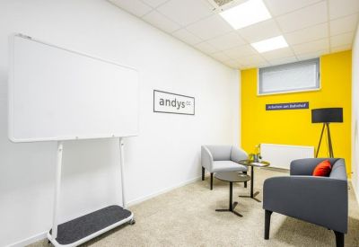 Modern lounge area with grey furniture, a mobile whiteboard, and a bright yellow feature wall.