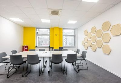 Spacious meeting room featuring a large white table, grey chairs, and honeycomb wall decor.